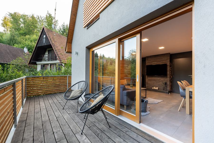 Dřevěný balkon s křesly a výhledem na les a sousední chatu