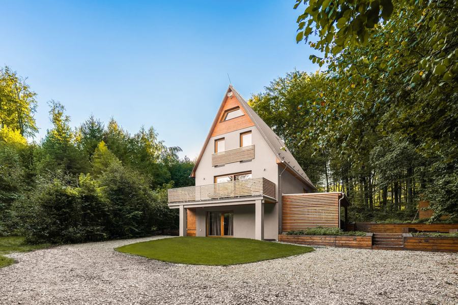 Chata ve tvaru A s balkonem, před ní štěrková příjezdová plocha