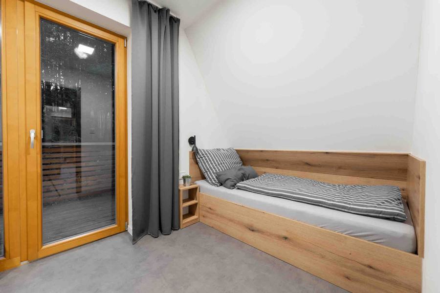 Jednolůžko u prosklených dveří na balkon a dubová komoda