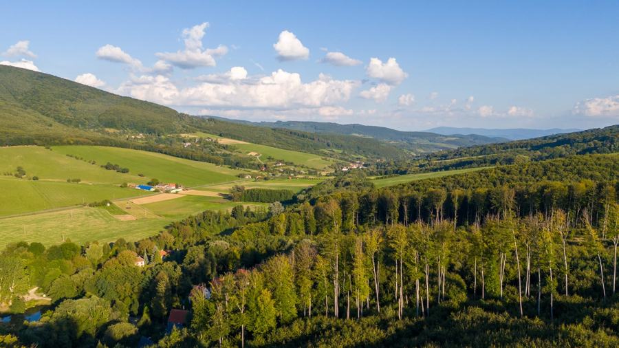 Zvlněná krajina Bílých Karpat s loukami a lesy, v údolí chatová osada